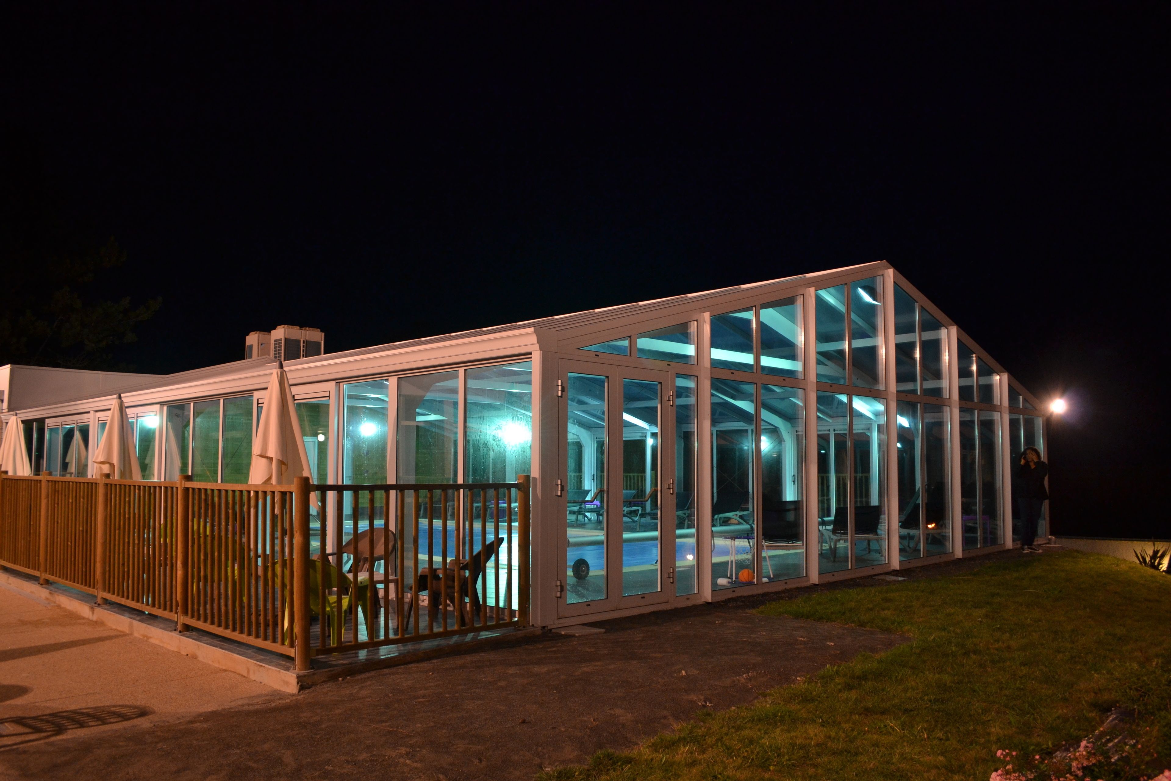 A modern glass-enclosed building with a fenced patio area.