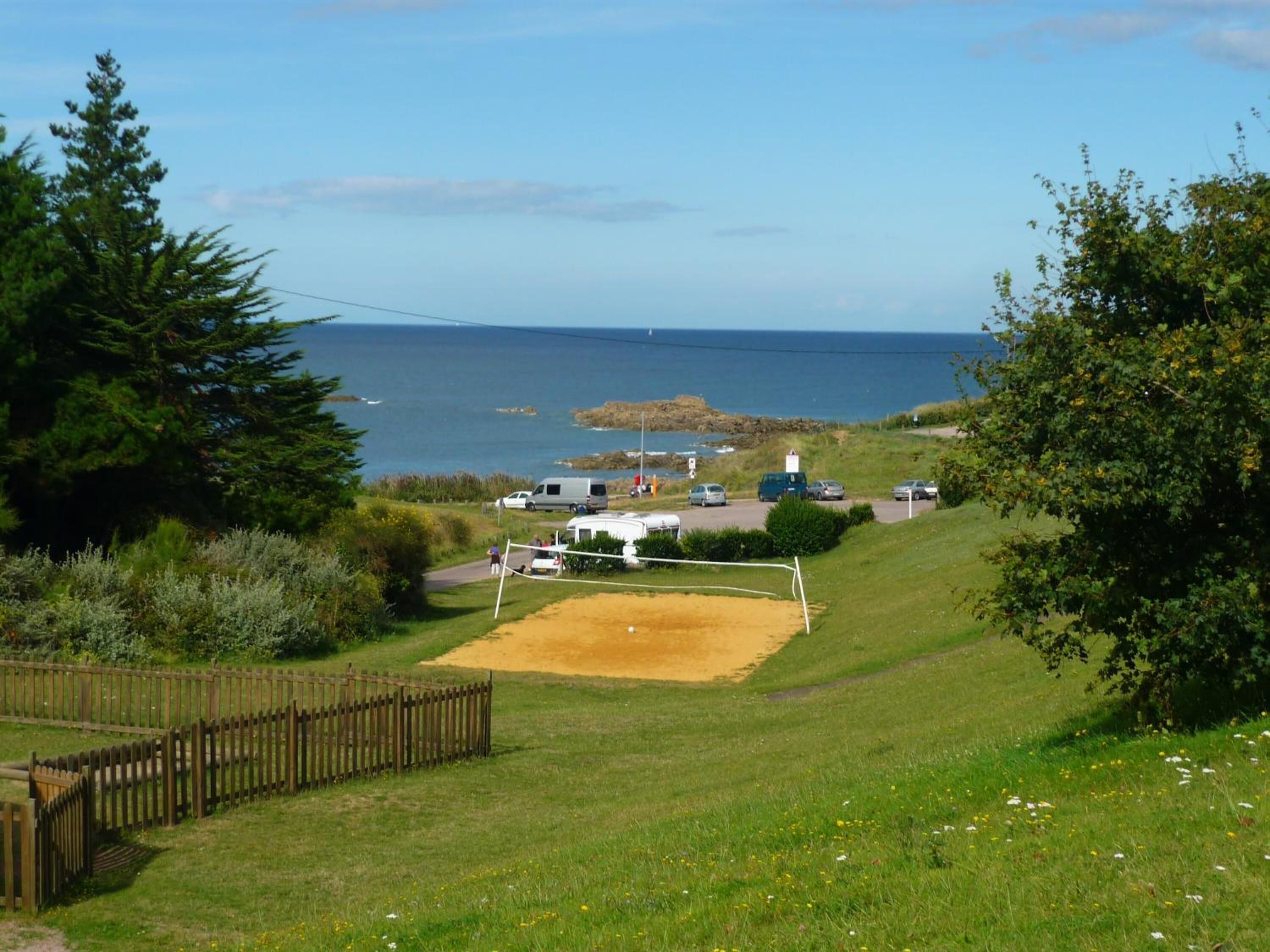 A grassy area with a volleyball net, a fenced section, and a body of water in the background.