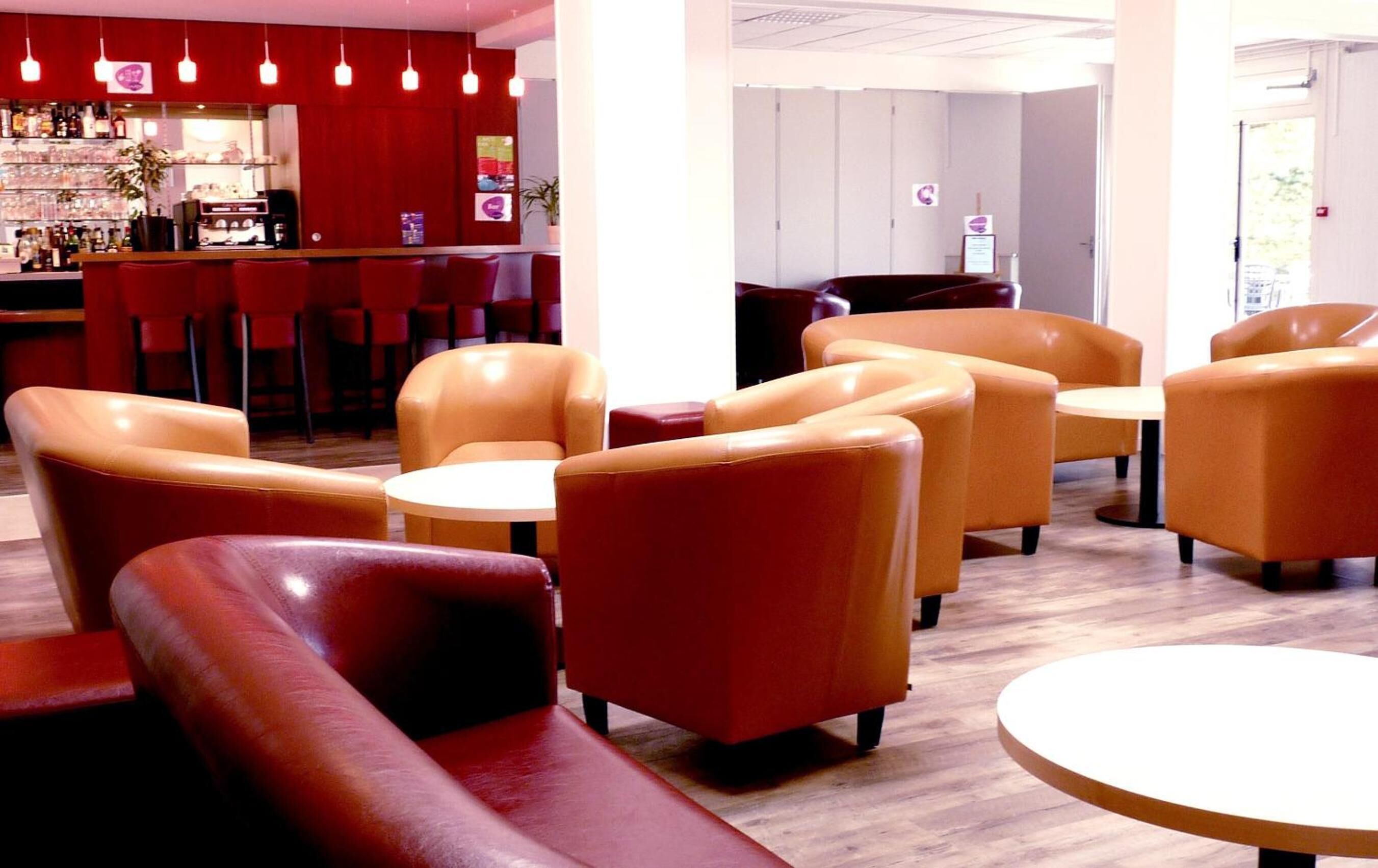 A bar area with red seating and a counter, and a seating area with tan chairs and round tables.