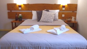 A neatly made bed with a grey duvet, two rolled white towels, and a wooden headboard with wall-mounted lights. - VVF Jura Les Rousses, Prémanon (Premanon)