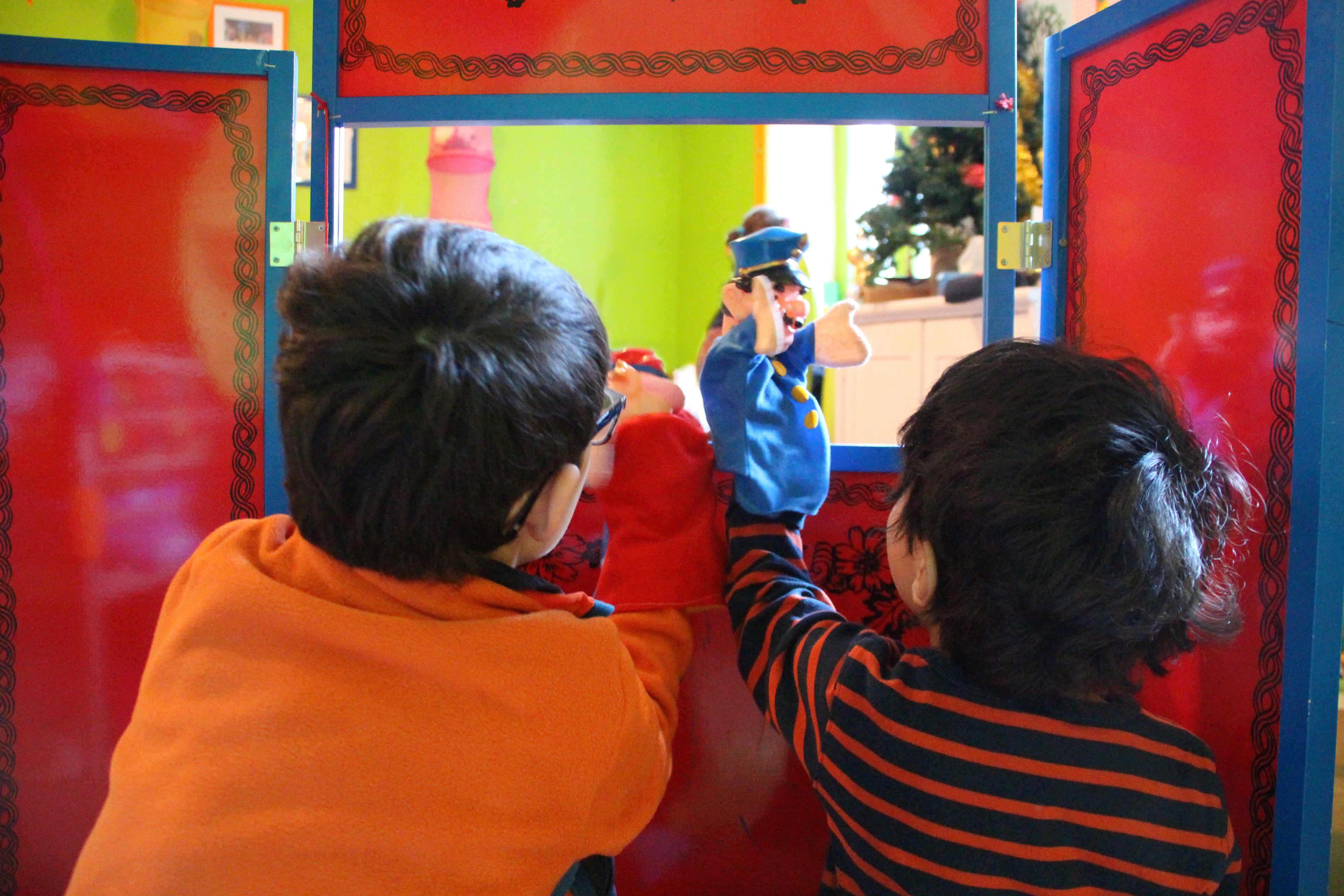 A child in an orange sweater looking through a window at a person in a blue uniform.