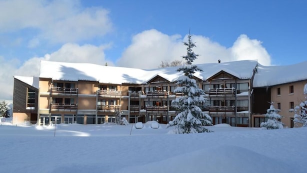 A multi-story hotel with a snow-covered roof and balconies, surrounded by snow. - VVF Jura Les Rousses, Prémanon (Premanon)