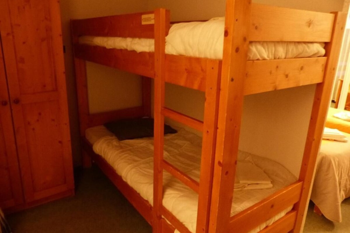 A bunk bed room with a wooden wardrobe and a bed with white bedding.