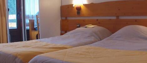 A double bed with a wooden headboard and a nightstand, a window with curtains, and a view of the outdoors.
