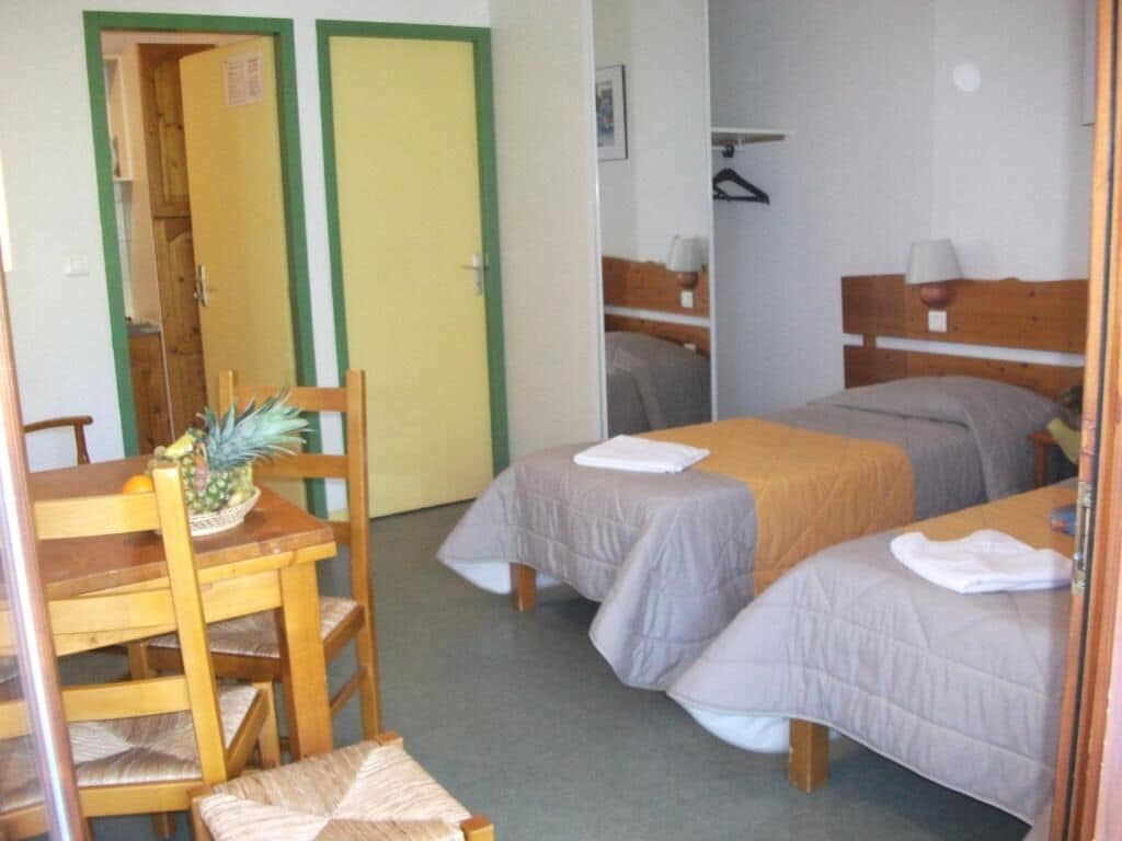Une chambre avec deux lits, une table en bois sur laquelle se trouve un ananas, et une chaise.