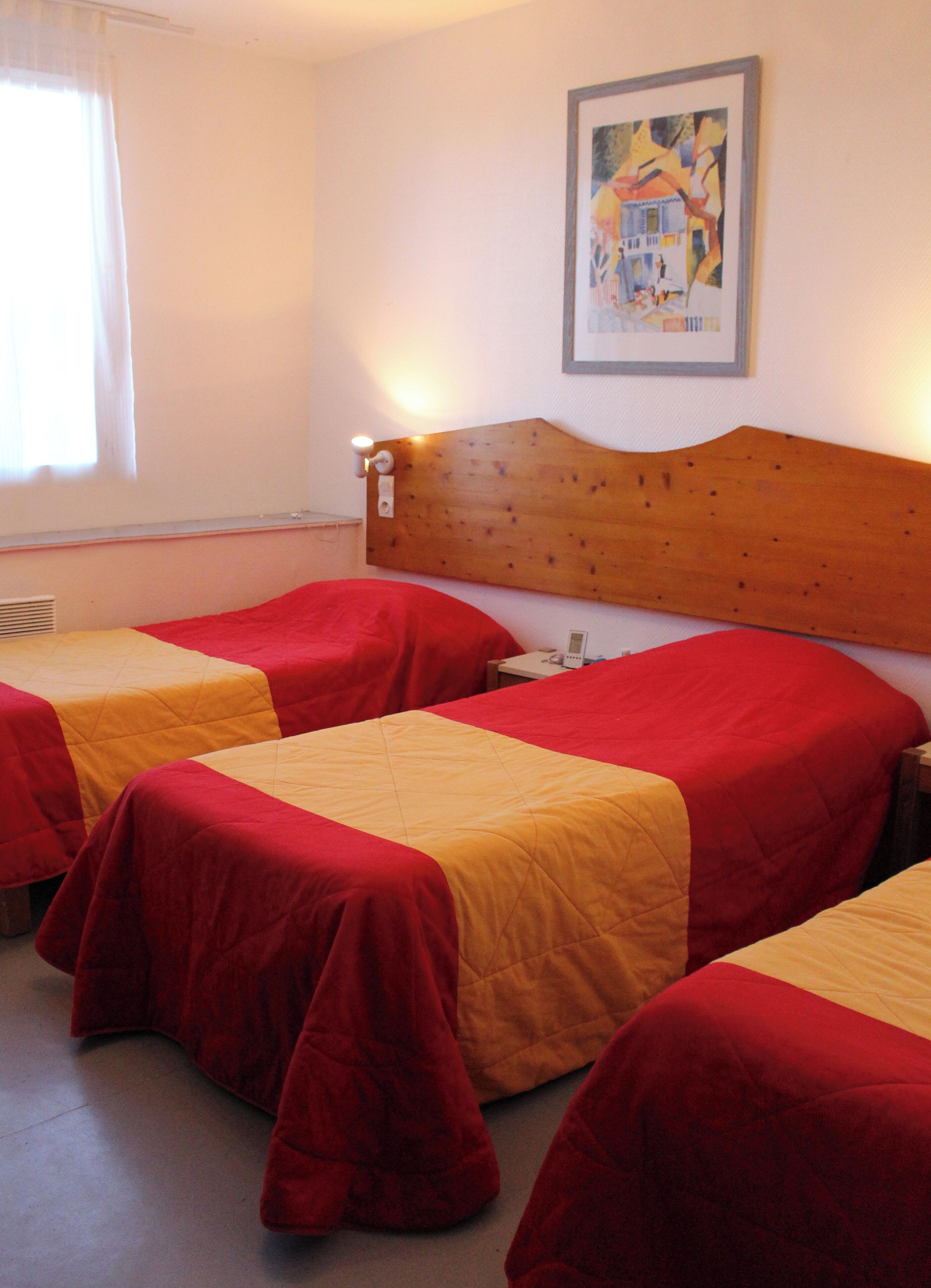 Una habitación de hotel con dos camas, cada una con ropa de cama roja y amarilla. Cuenta con un cabecero de madera, una lámpara de pared y un cuadro en la pared.