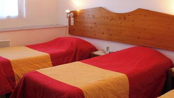 Una habitación de hotel con dos camas, cada una con ropa de cama roja y amarilla. Cuenta con un cabecero de madera, una lámpara de pared y un cuadro en la pared.