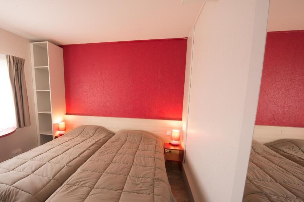 Une chambre avec deux lits, un mur rouge et un plafond blanc.