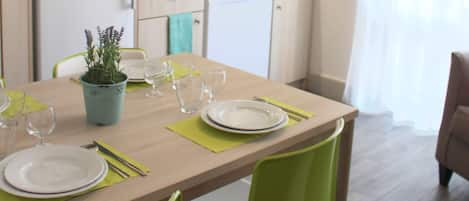 A compact kitchen with a microwave, refrigerator, and dishwasher. There is a dining table set with plates, glasses, and a potted plant.