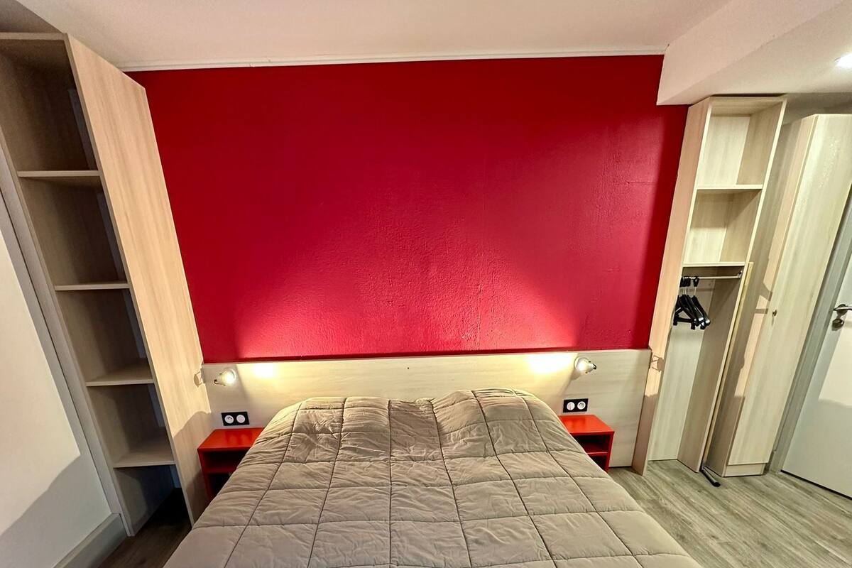 Een slaapkamer met een bed, een rode wand, een houten vloer en een kledingkast.