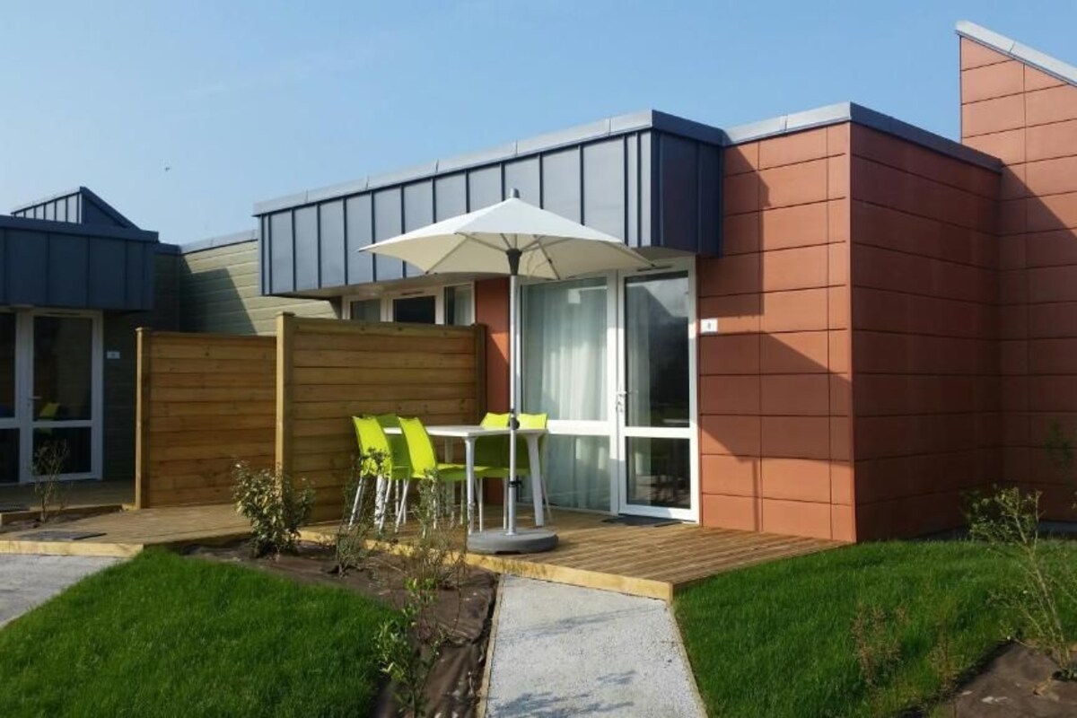 Ein modernes Haus mit Terrasse, einer Holzterrasse und einer Glastür, die zu einem Raum führt.