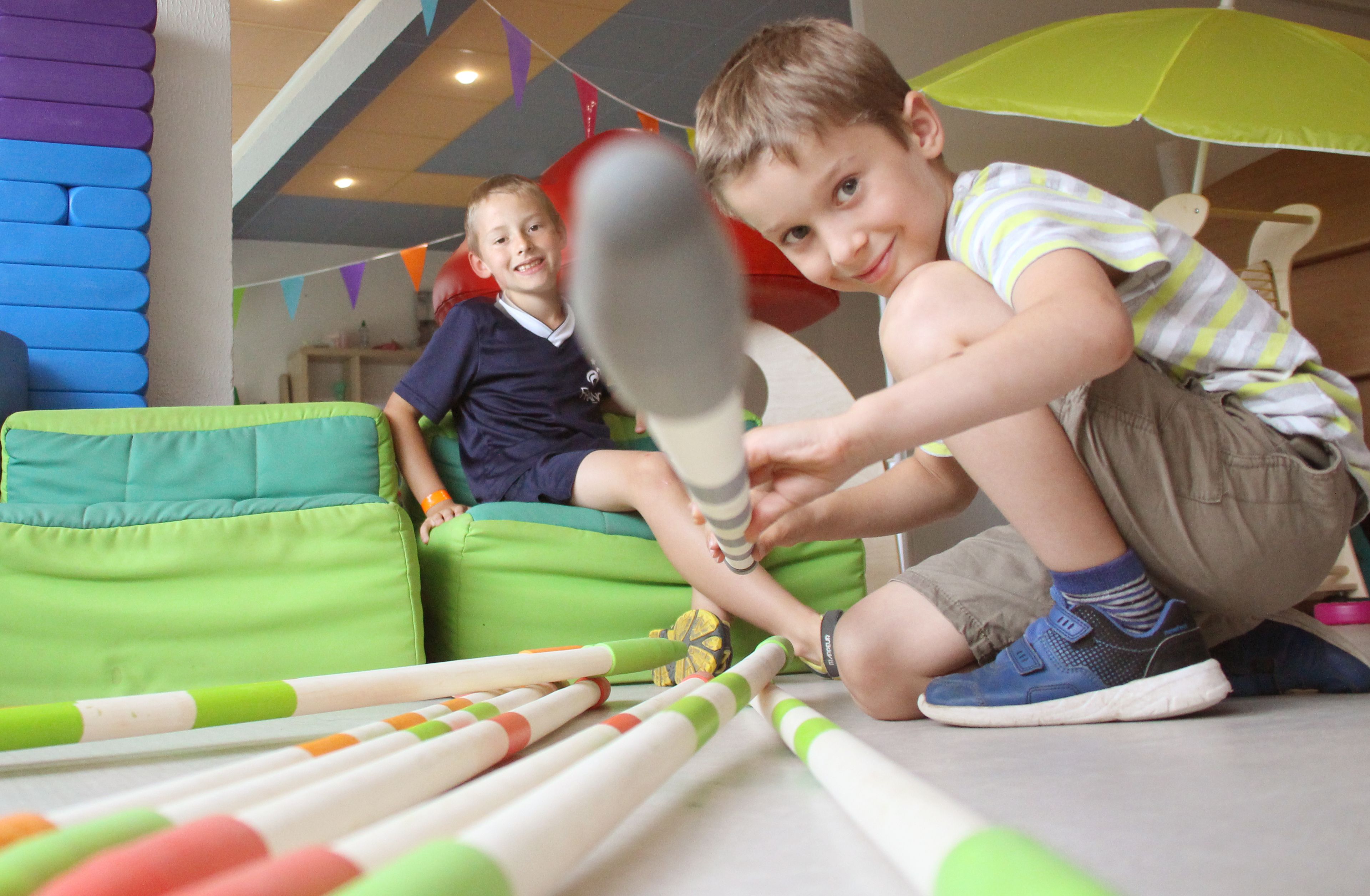 Children playing with bat and ball, green bean bag chairs, and colorful toys on the floor.