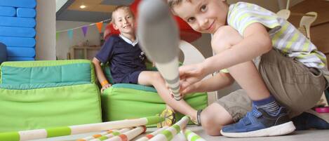 Children playing with bat and ball, green bean bag chairs, and colorful toys on the floor.