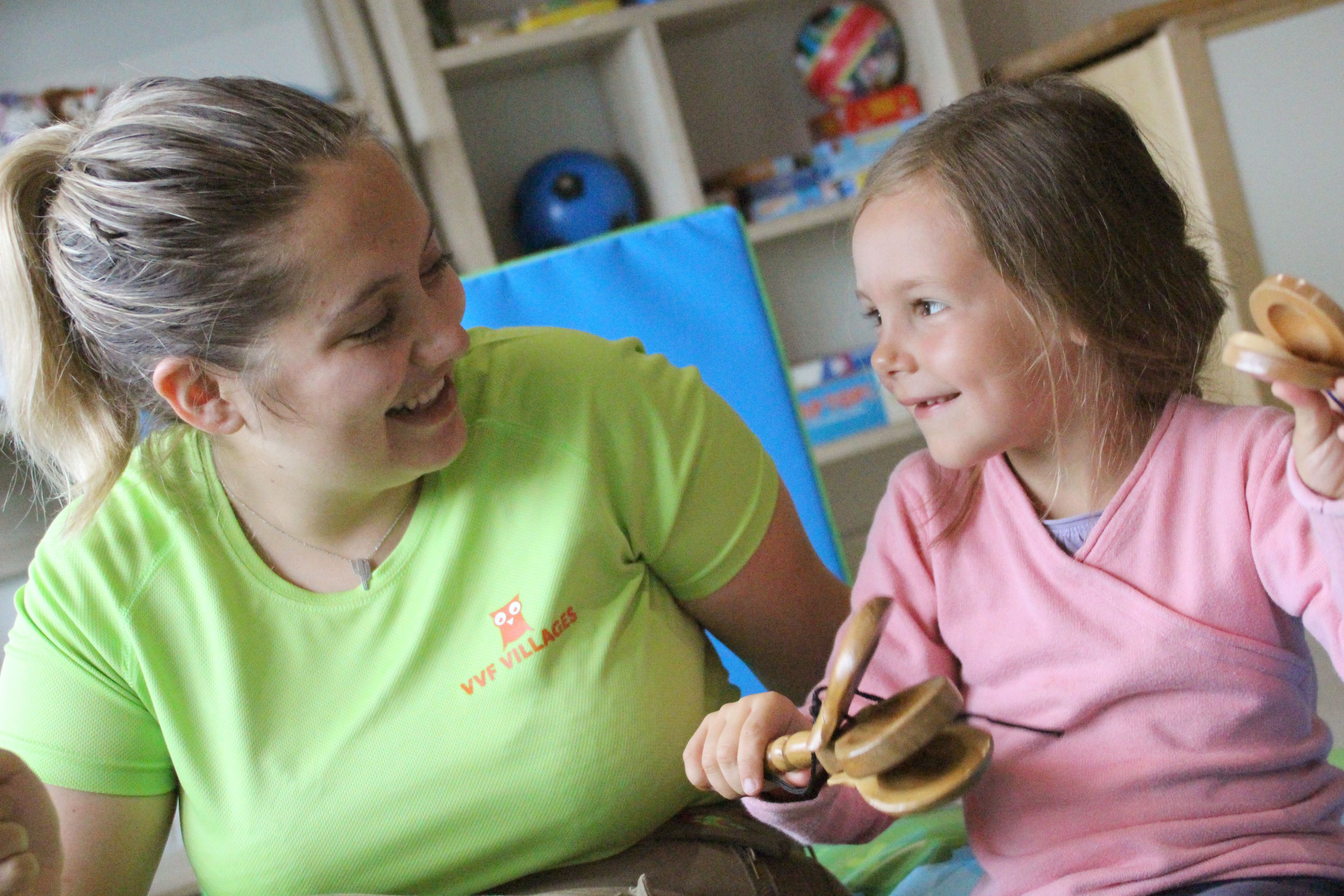 A woman in a green shirt and a child in a pink shirt sitting at a table.