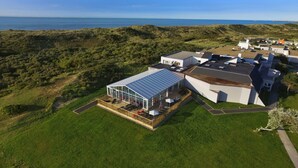 A modern building with a glass conservatory, surrounded by lush greenery and a view of the sea. - VVF Blériot-Plage (Sangatte)