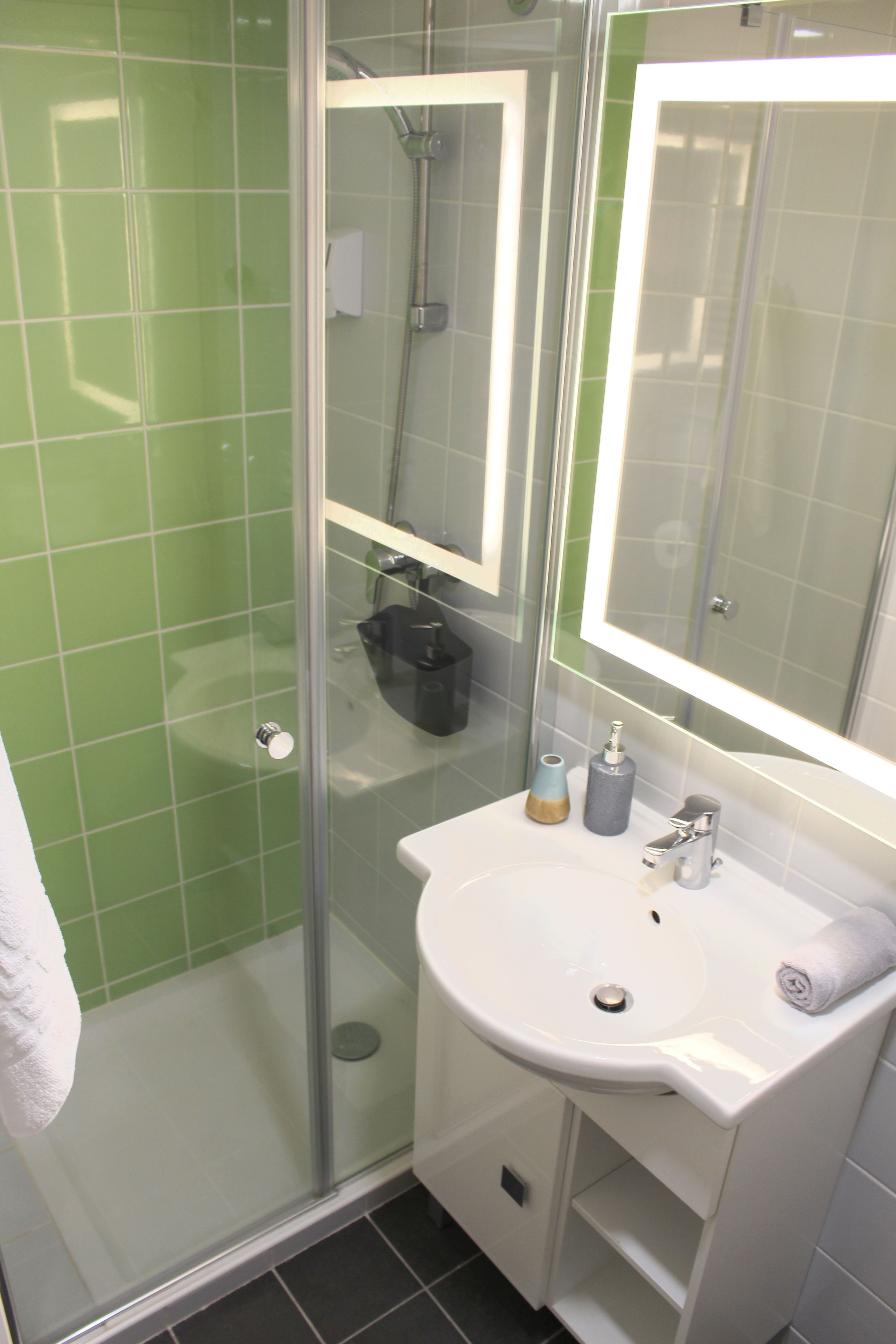 Een badkamer met een douchecabine van glas, een wit wastafelmeubel en een spiegel erboven.