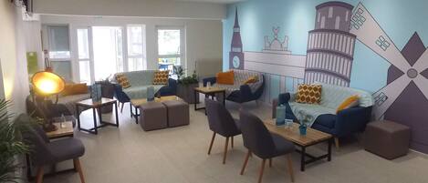 Un espace de détente moderne, avec des canapés, des fauteuils et une table basse. On y trouve également des plantes en pot et une fresque murale.