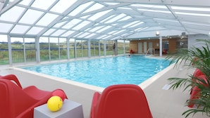 An indoor swimming pool with clear glass ceilings, red chairs, and a yellow ball on a table. - VVF Blériot-Plage (Sangatte)
