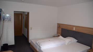 A hotel room with a single bed, a bedside table with a phone, and a small table with a remote control.
