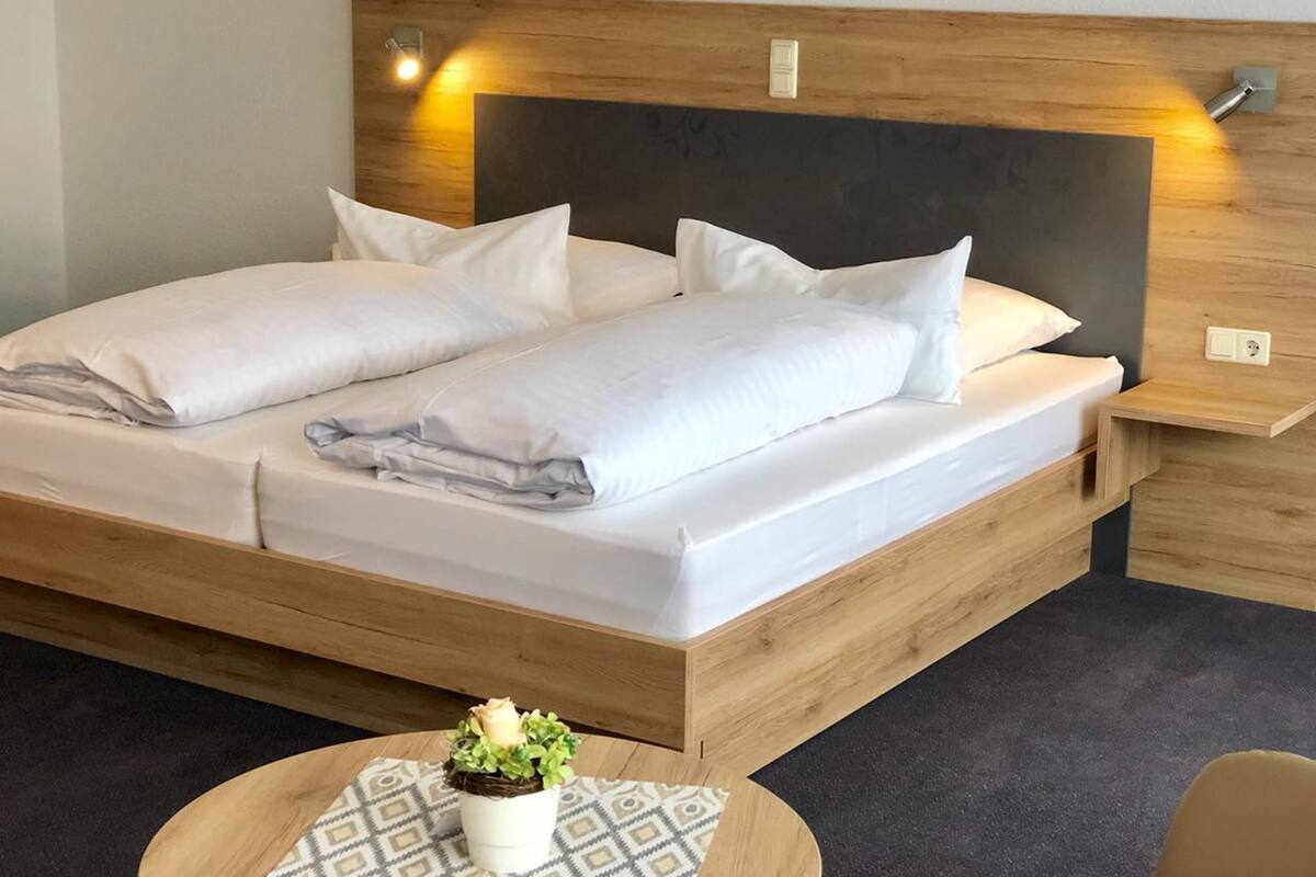 A double bed with a wooden headboard, two bedside tables, and a small round table with a plant.
