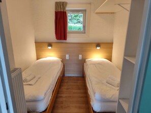 Une petite pièce étroite avec deux lits, une petite fenêtre avec des rideaux et un radiateur.