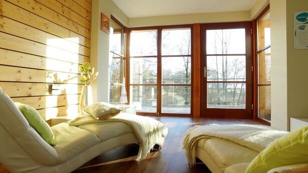 A cozy room with a wooden wall, a sofa, a window with a view of trees, and a door.