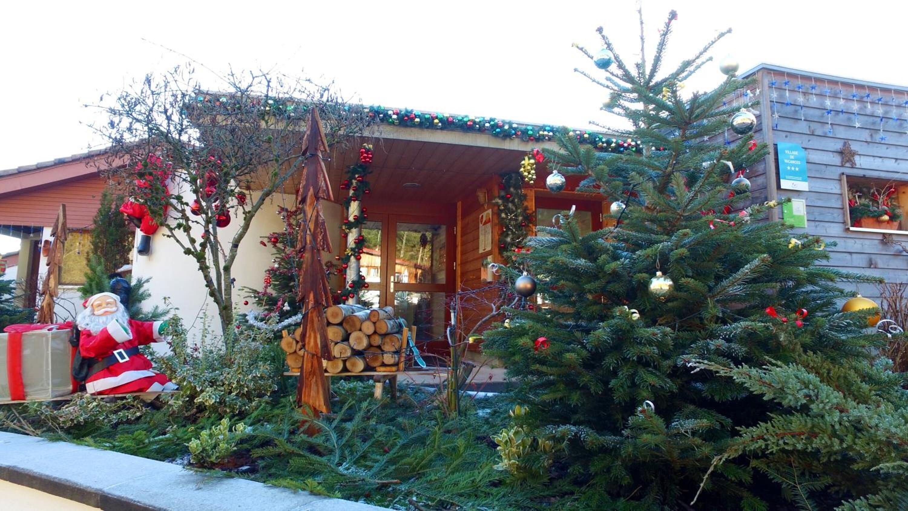 A wooden cabin with a porch decorated with Christmas trees and ornaments, a Santa Claus figure, and a sign indicating vacancies.