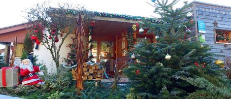 A wooden cabin with a porch decorated with Christmas trees and ornaments, a Santa Claus figure, and a sign indicating vacancies.
