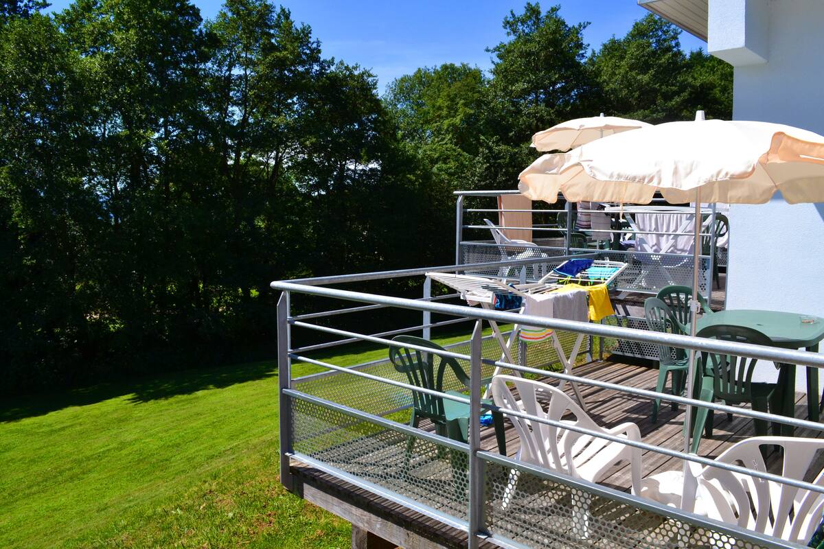 Eine Terrasse mit Gartenmöbeln, darunter Stühle und Tische, umgeben von einem Metallgeländer.