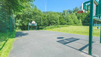 A basketball court with a hoop, surrounded by a green fence and trees.