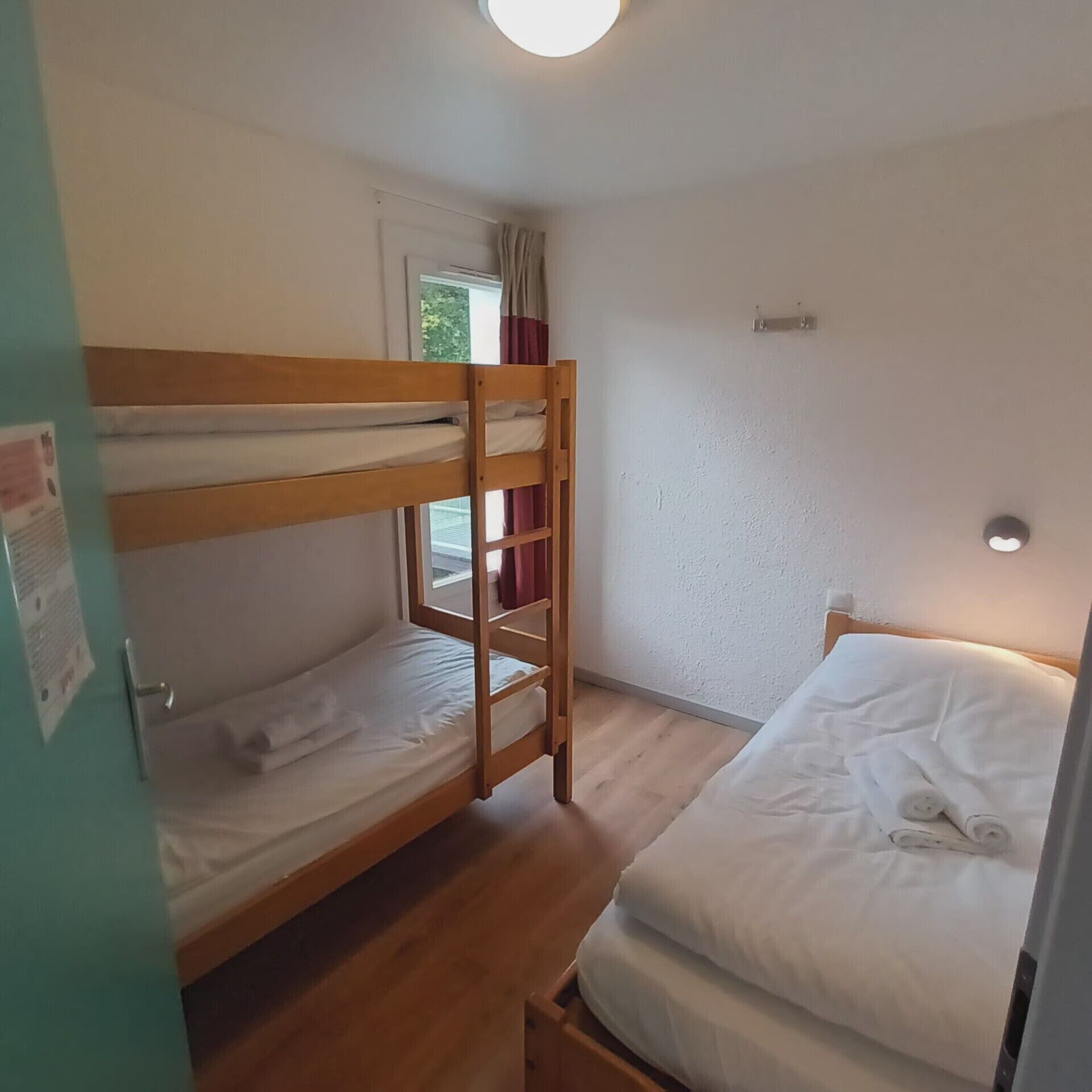 Une chambre avec un lit superposé, une fenêtre, une porte et un luminaire.