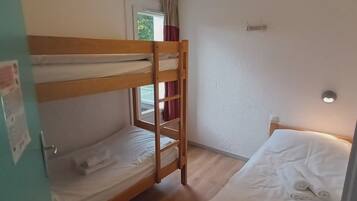 Une chambre avec un lit superposé, une fenêtre, une porte et un luminaire.