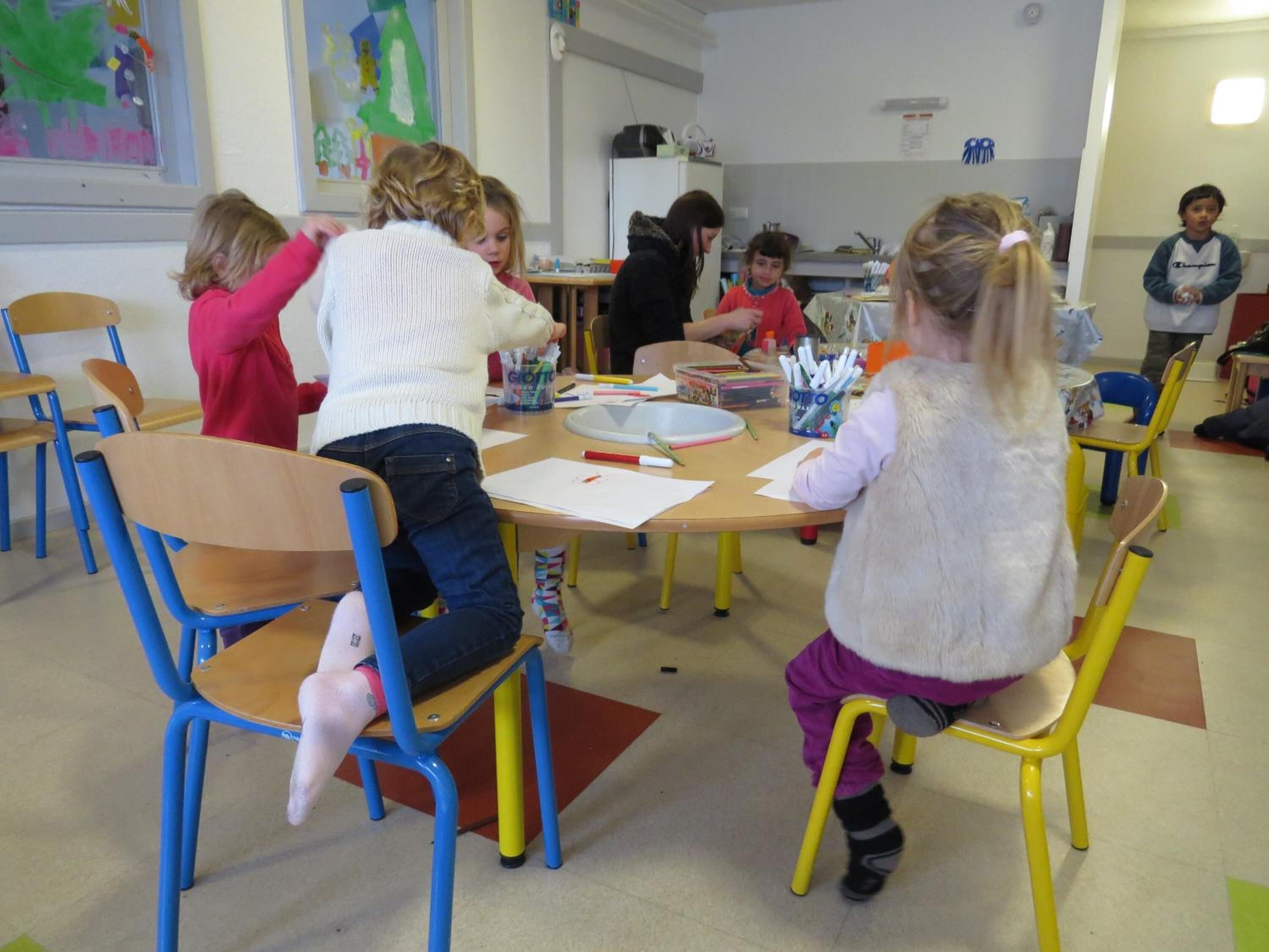 A classroom with children engaged in activities, wooden chairs, and tables with educational materials.