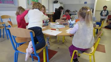 A classroom with children engaged in activities, wooden chairs, and tables with educational materials.