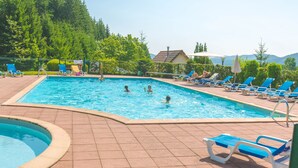 A swimming pool with people in the water, surrounded by lounge chairs and a tiled deck.