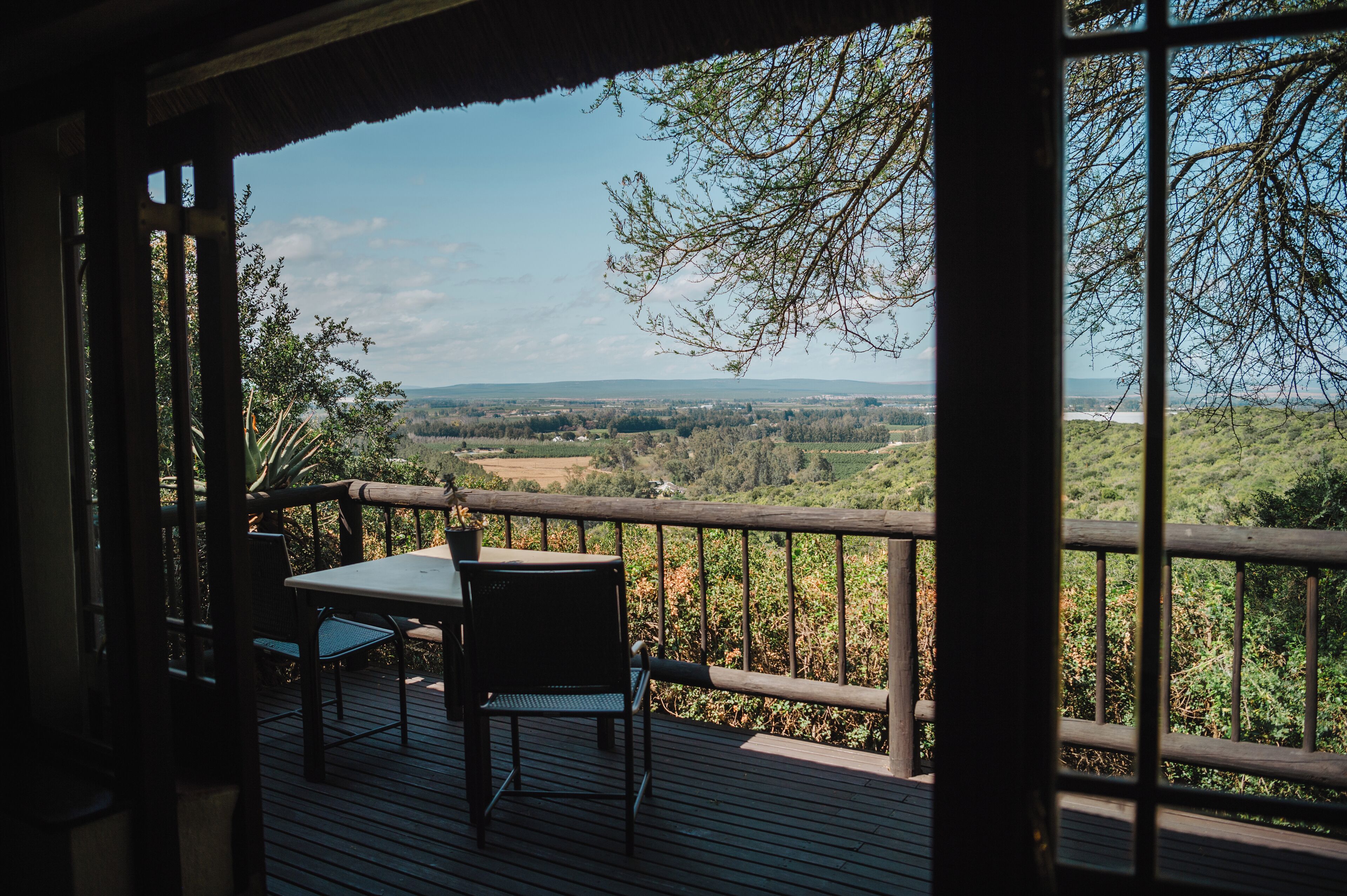 Una terraza de madera con una mesa y sillas, con vistas a un paisaje pintoresco con árboles y colinas.