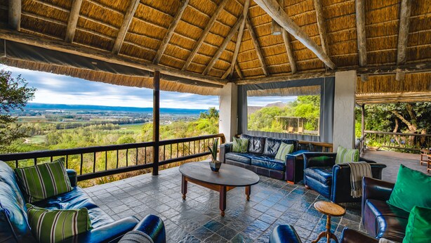 Een overdekt terras met rieten dak, een loungeset, een bijzettafeltje en uitzicht op het landschap.