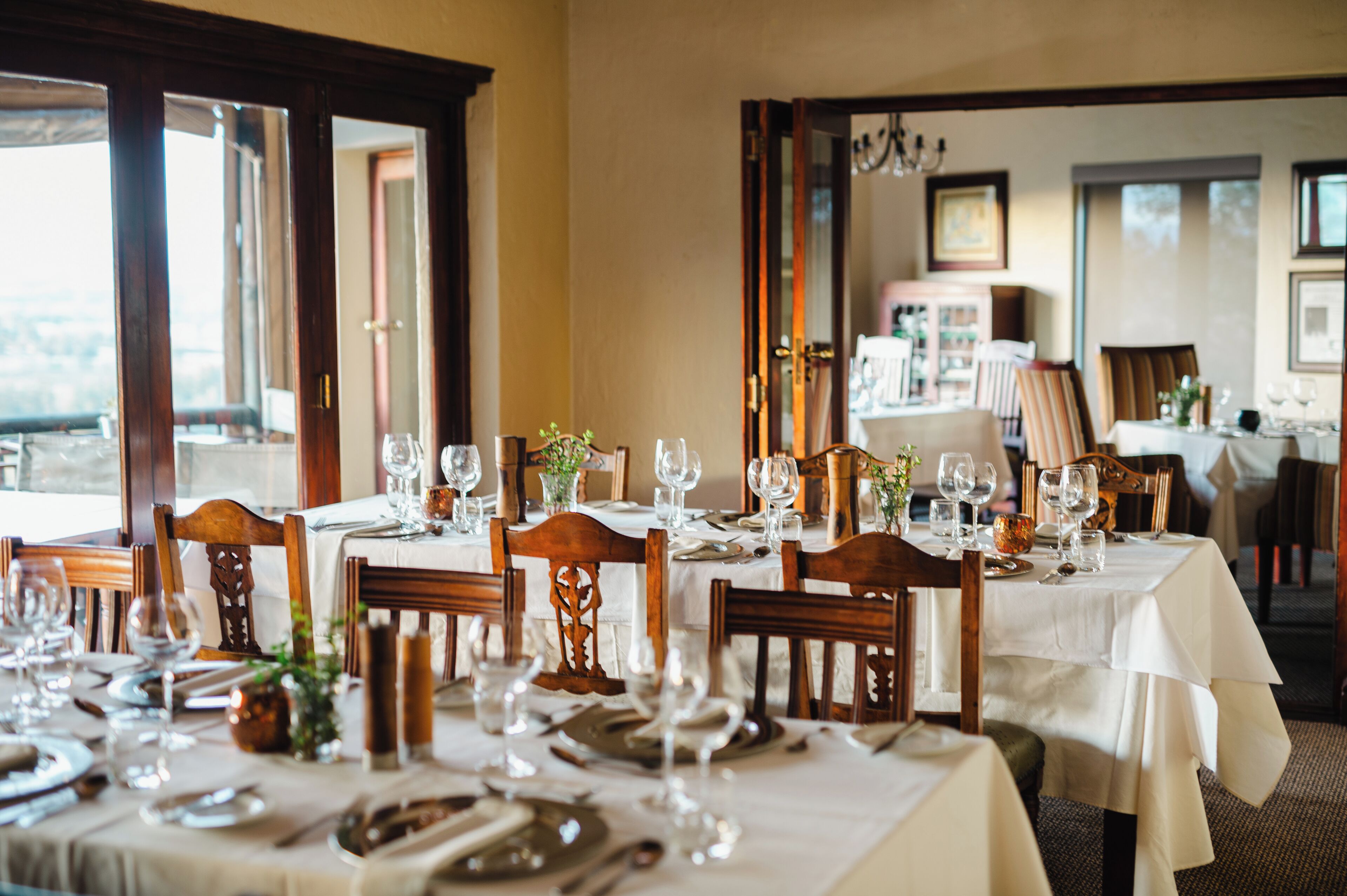 A dining area with tables set for a meal, featuring wooden chairs and white tablecloths.