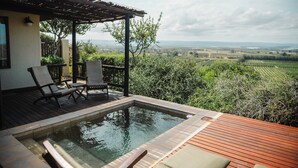 Een houten terras met een jacuzzi, twee loungestoelen en een pergola met uitzicht op een wijngaard.