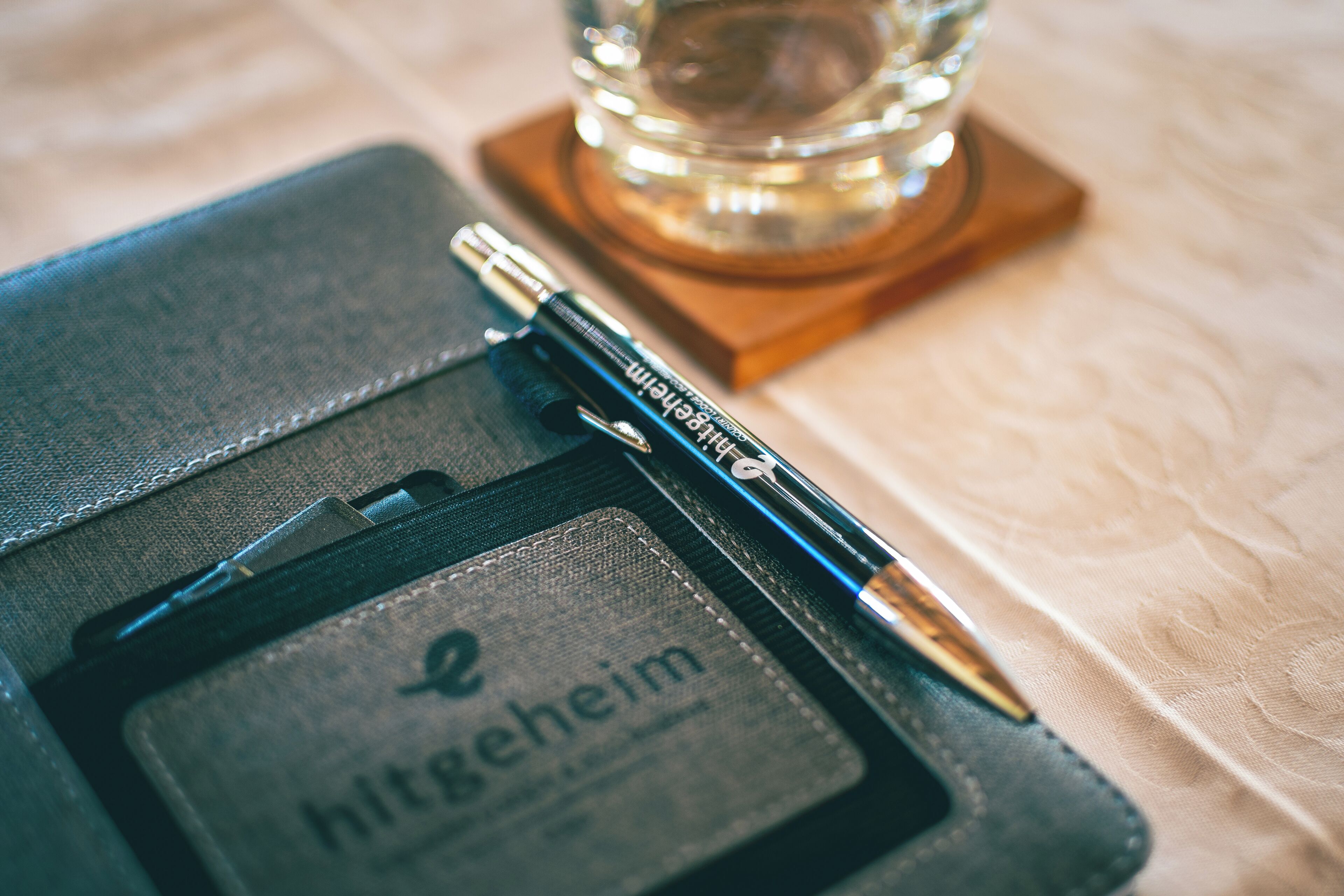 A notebook with a pen and a coaster with a glass.