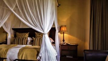 A four-poster bed with a canopy, a bedside table with a lamp, a chair, and a view of greenery outside.