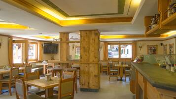A restaurant with wooden furniture, a TV mounted on the wall, and a counter with a display case.