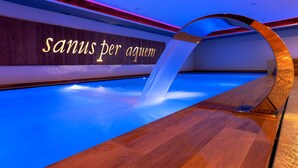 A modern indoor pool area with a wooden floor and a neon sign reading "Sanus per aquem". - Hotel Amerikan (Livigno)