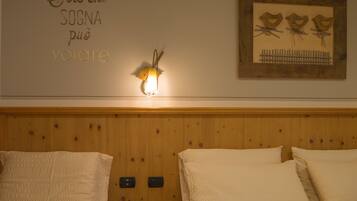 Een hotelkamer met een houten hoofdeinde, een wandlamp, een lijst met een afbeelding van vogels en een bord met Italiaanse tekst.