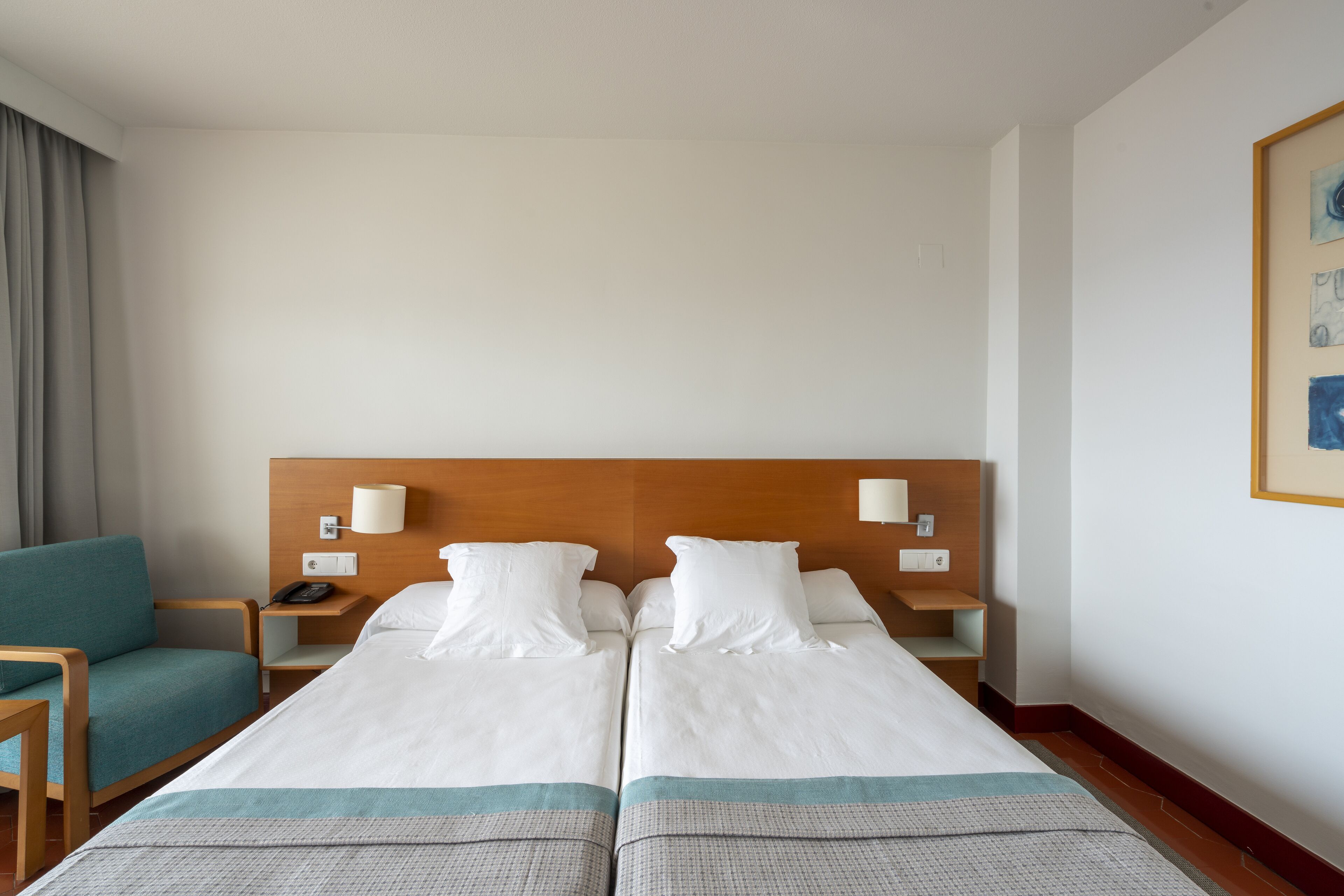 Habitación de hotel con dos camas, un escritorio, una silla y un cuadro en la pared.