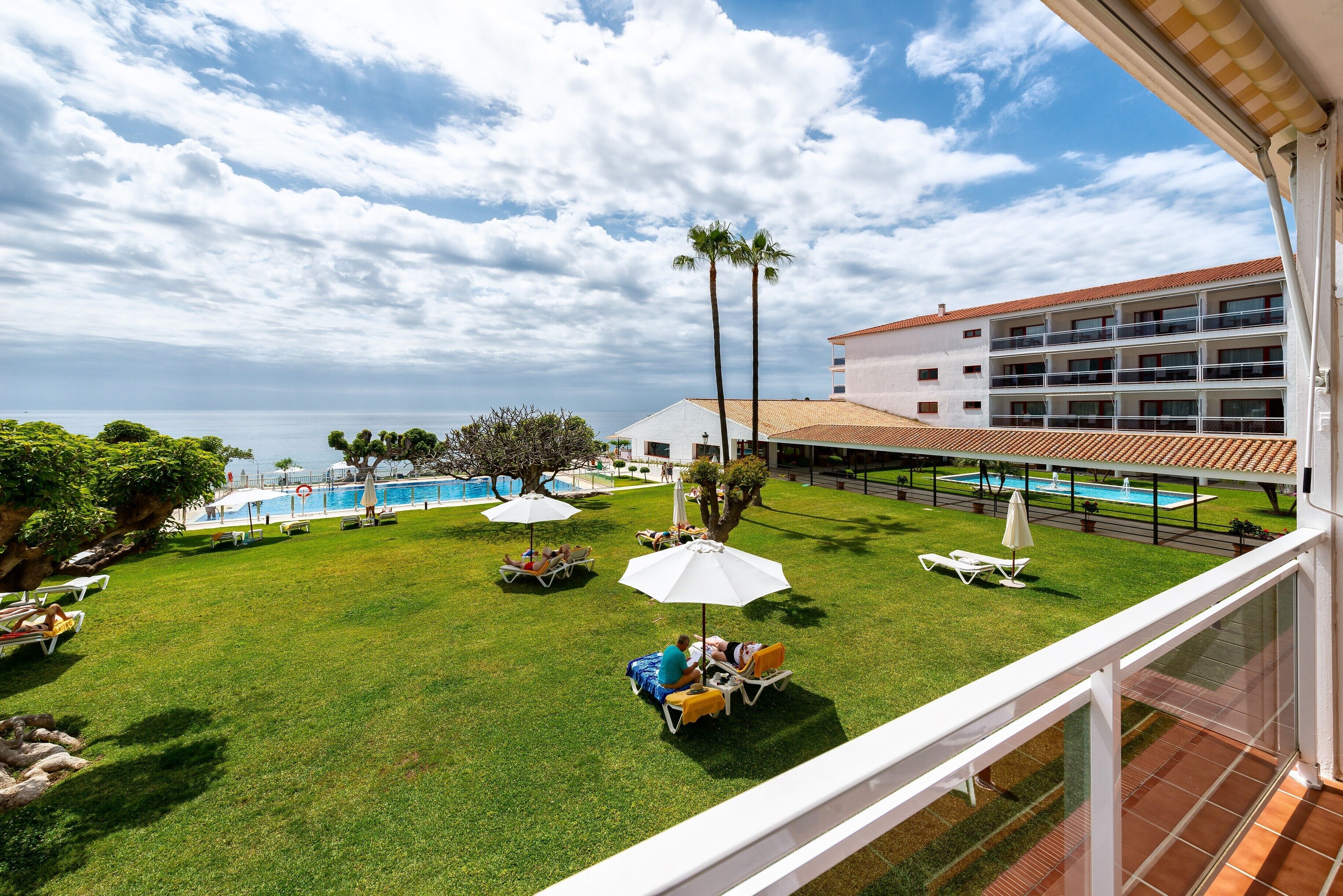 Un patio de hotel con piscina, tumbonas y sombrillas.
