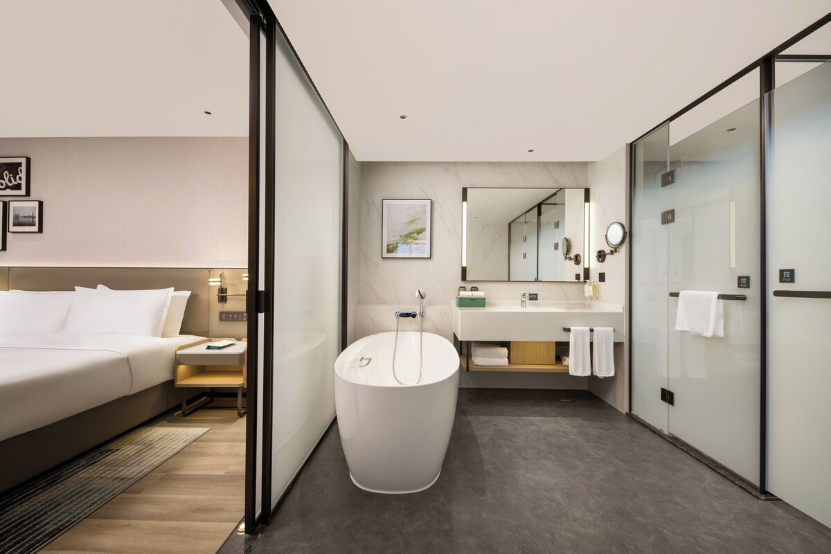 Une chambre d’hôtel moderne dotée d’un grand lit, d’une baignoire sur pieds, d’une coiffeuse avec un miroir et d’une douche à parois de verre.