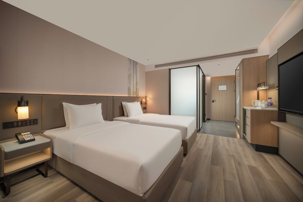 Une chambre d’hôtel avec deux lits, un bureau avec un téléphone, une télévision et une kitchenette.
