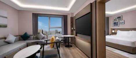 A modern hotel room with a sofa, a dining table, a bed, and a large TV.