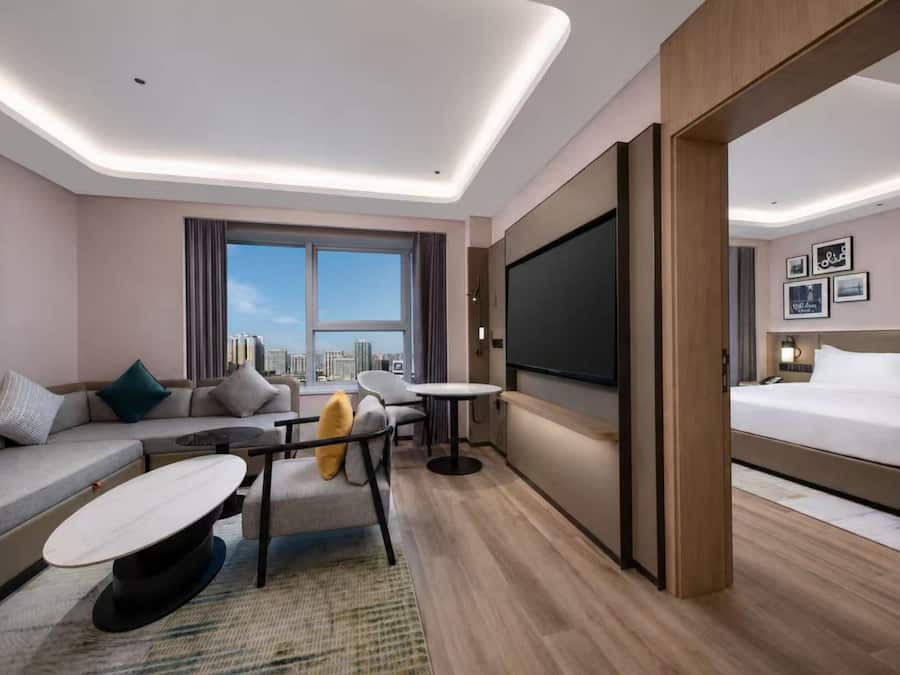 Habitació d'hotel moderna amb sofà, taula de menjador, llit i un televisió gran.